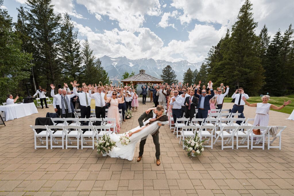 wide angle of couple kissing and guests cheering during wedding ceremony at silvertip resort in Canmore