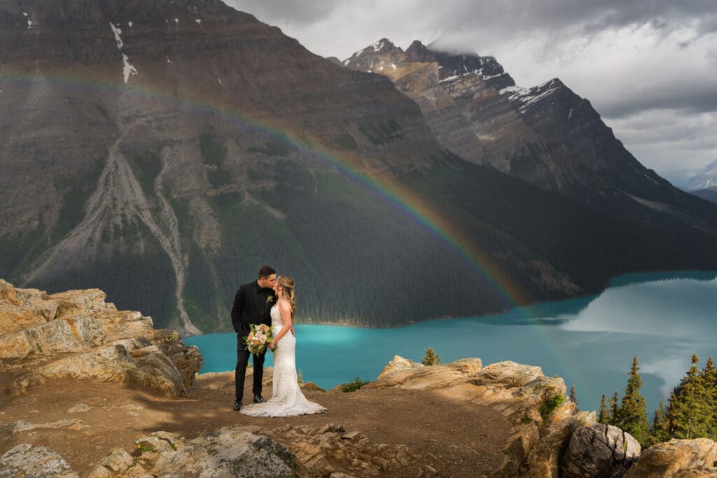 couple kisses under a rainbow at Peyto Lake in Banff